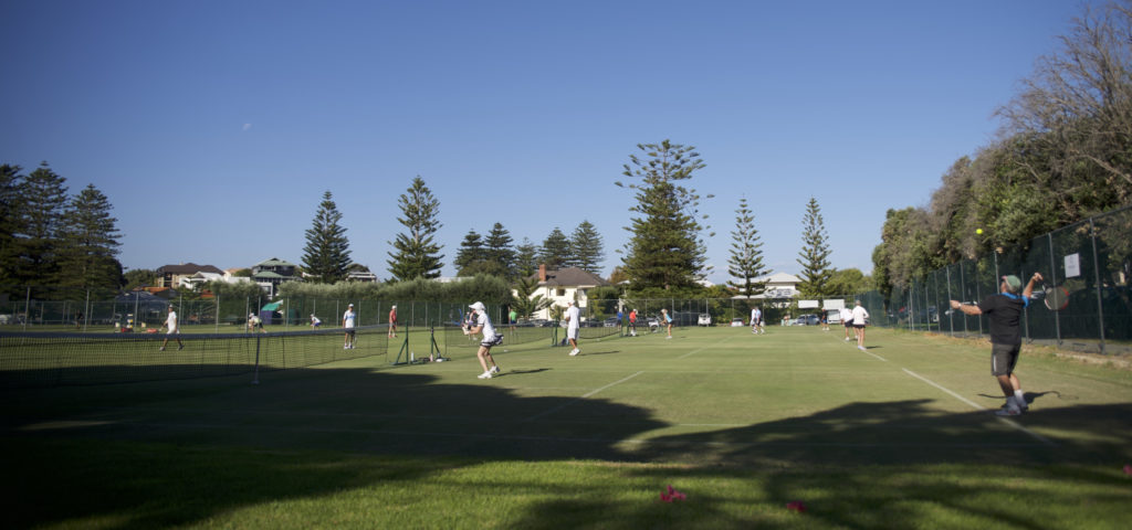 People playing tennis on the grass, man serving in foreground